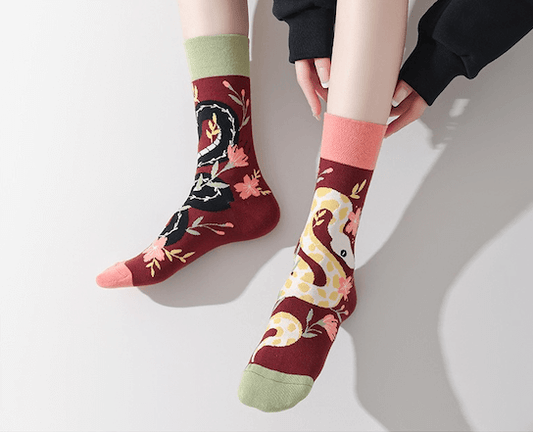 Paire de chaussettes fantaisie dépareillées bordeaux avec motifs serpent noir et serpent clair entourés de fleurs colorées