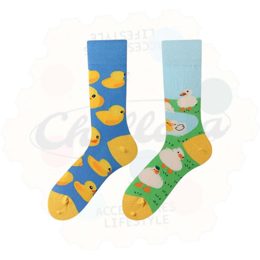 Chaussettes fantaisie dépareillées : une chaussette bleue avec des canards jaunes façon jouets de bain, l’autre verte représentant des canetons blancs près d’un étang sur fond de prairie.
